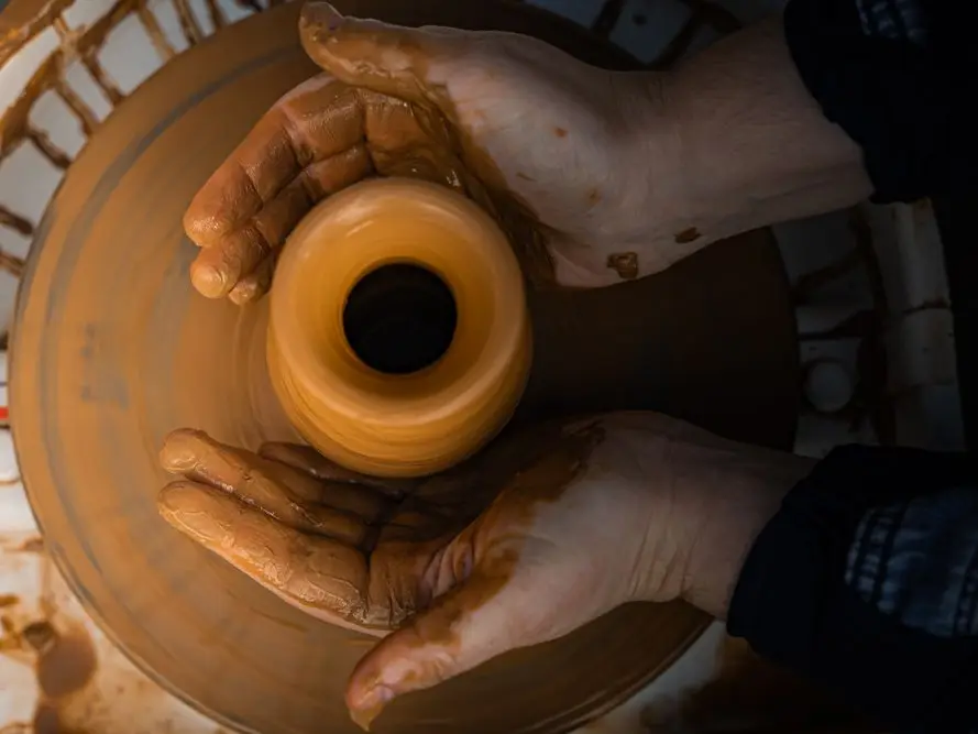 Clay-covered hands centering a pot on a spinning wheel