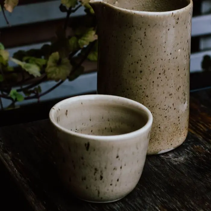 A speckled stoneware jug and cup on a dark wooden table
