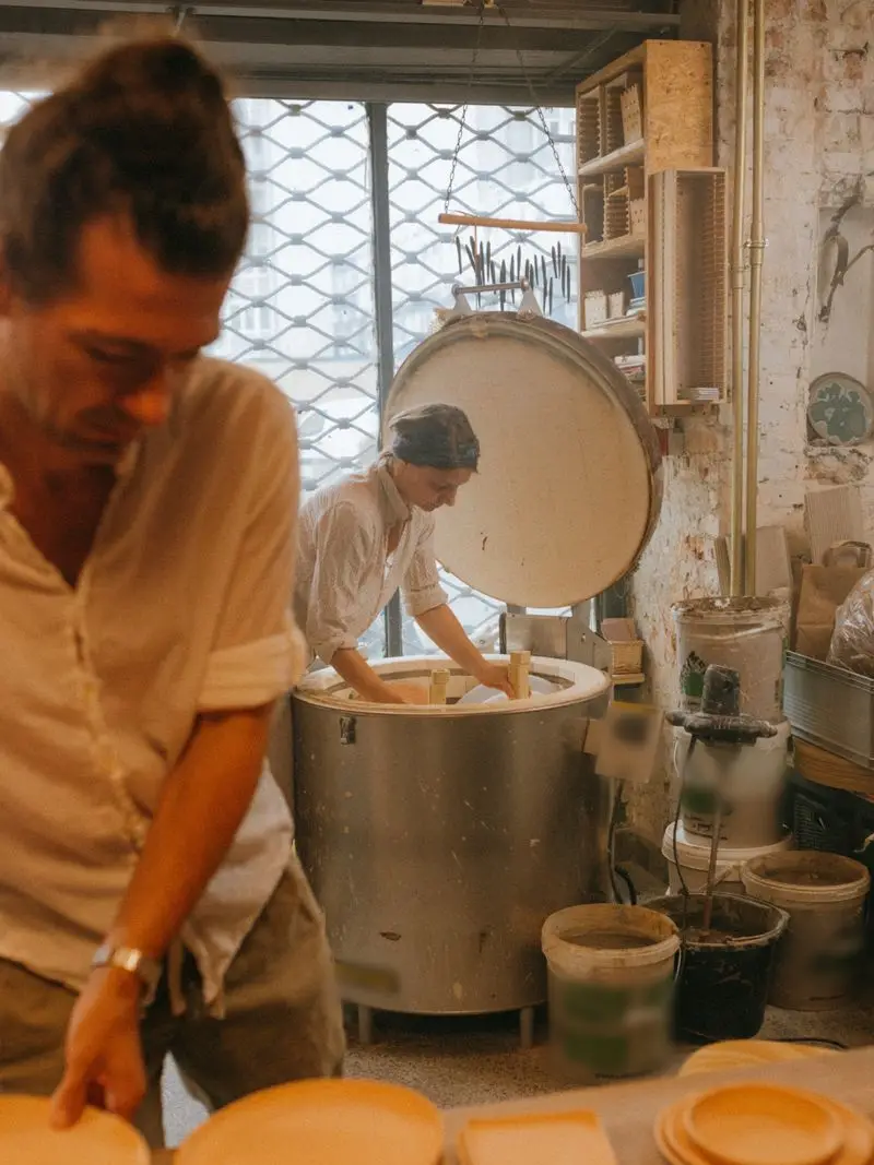 Two potters at work in a sunny studio, one loading an open kiln